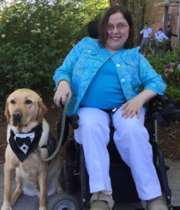 Another photo of a service dog, this time wearing a bandana that looks like the top of a formal tux, assisting a woman attending an event.